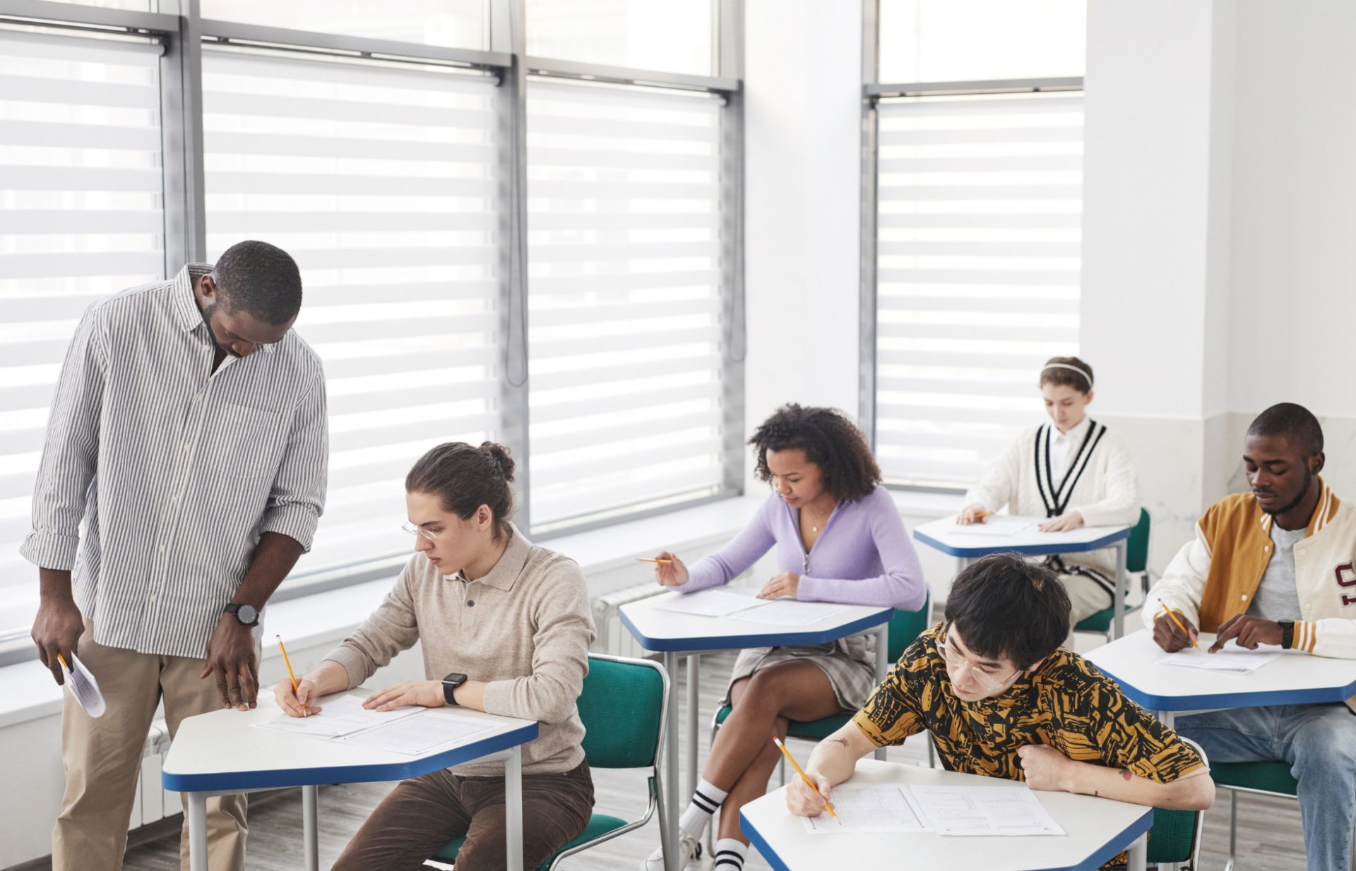 teacher in classroom watches student writing.