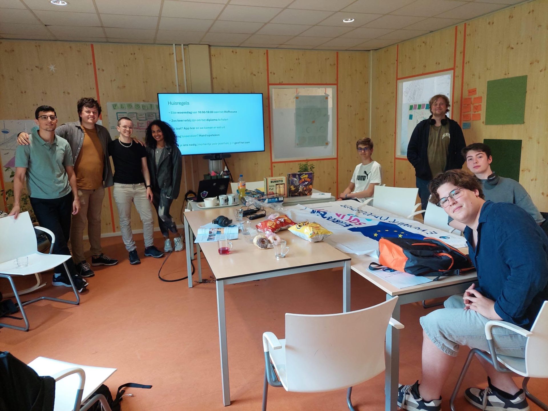 Groep jongeren en begeleiders in een klaslokaal tijdens een bijeenkomst van l’Oiseau Bleu, met een presentatie op een scherm en materialen op tafel zoals laptops, snacks en een EU-vlag.